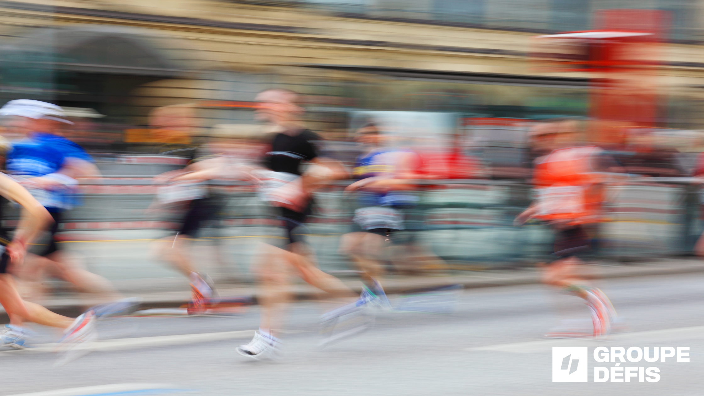 Blurred scene of marathon runners sprinting along a city street, colorful athletic gear in motion; Groupe Défis logo visible in the bottom-right corner.