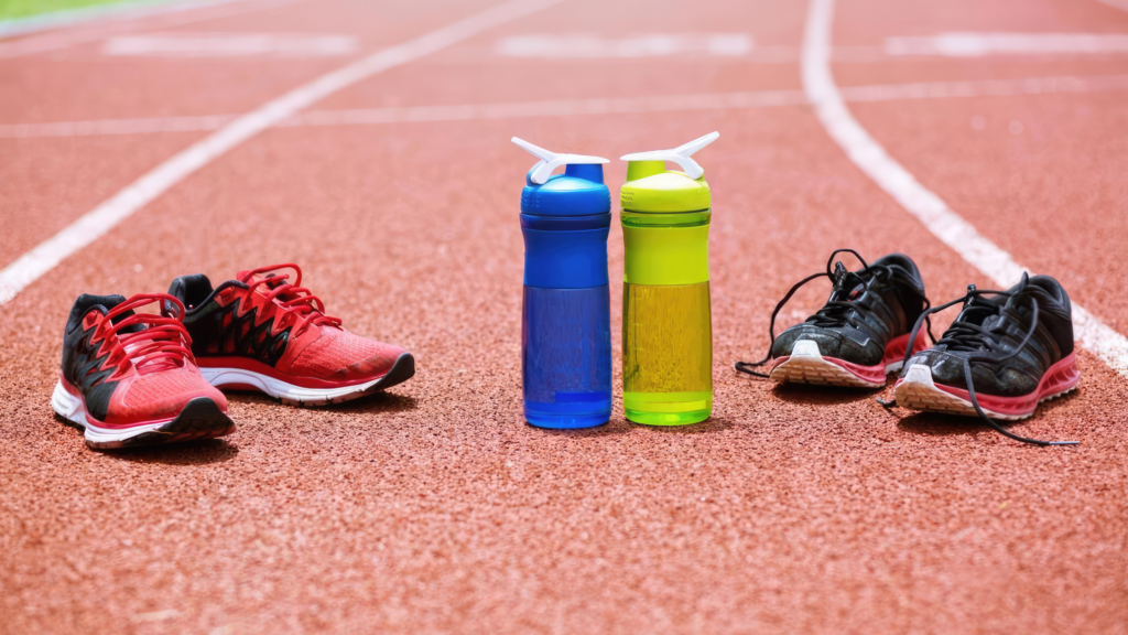 Red and black running shoes on a track with blue and lime water bottles placed between them on the lanes edge.